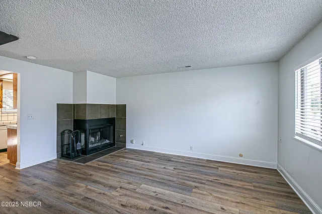 an empty room with wooden floor fireplace and windows