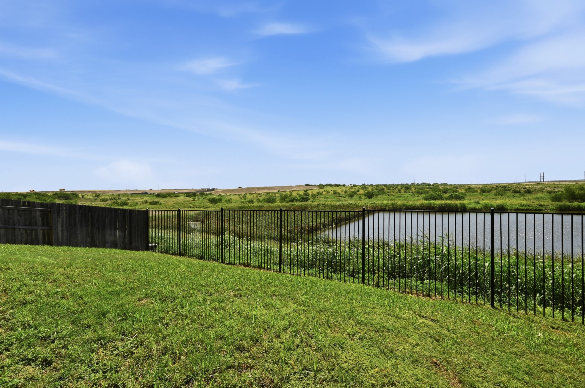 488 Pepperbark Loop Buda, TX 78610 - Photo 29 of 31 A tranquil pond view beyond a secure fence, offering a peaceful backdrop to the green yard.