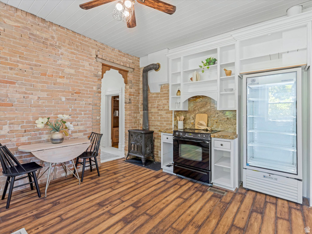 12825 South Fort Street Draper, UT 84020 - Photo 12 of 52 Exposed brick wall in kitchen area featuring wood-finish flooring, a wood-burning stove, and built-in shelving with an integrated range and counter space