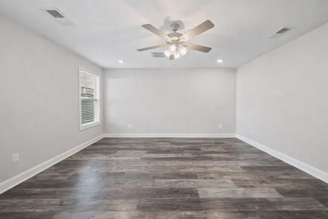 a view of an empty room with wooden floor and a ceiling fan