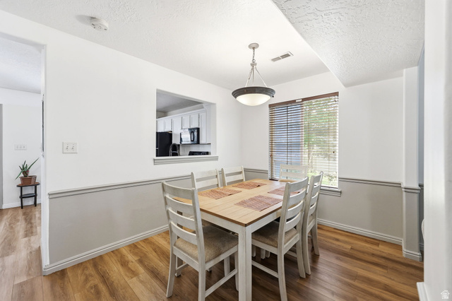 984 Independence Avenue Provo, UT 84604 - Photo 5 of 19 Dining area featuring wood-finish flooring, a contemporary ceiling light fixture, a window with blinds, and a pass-through opening to the kitchen