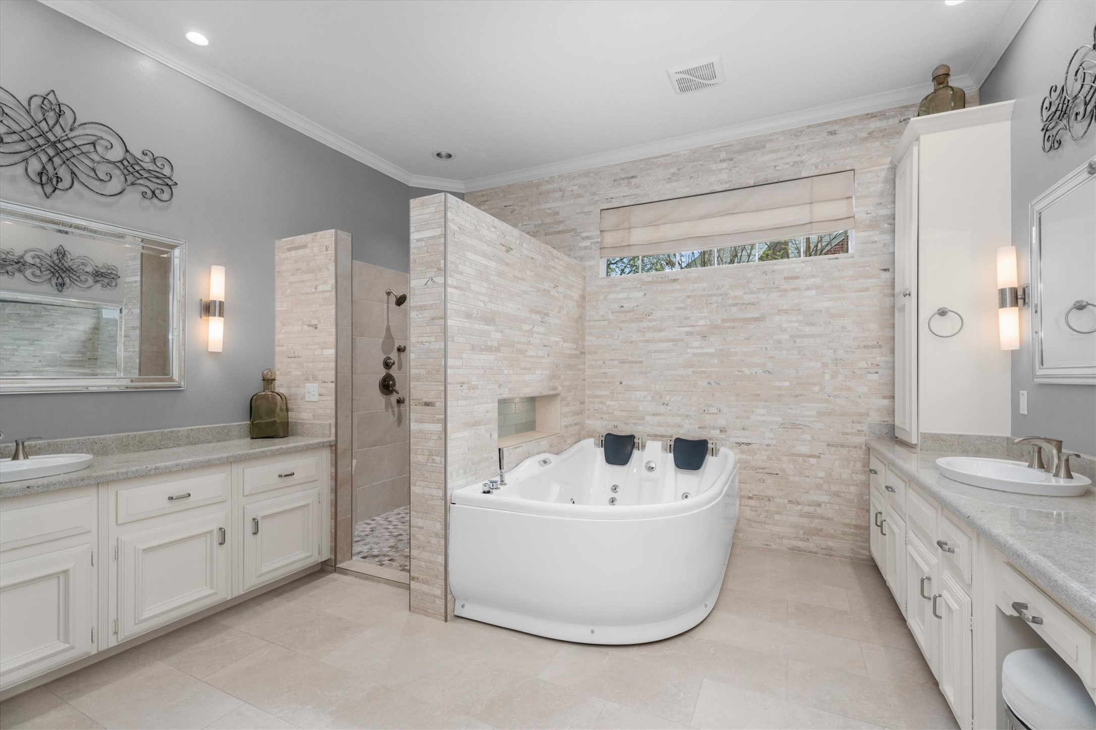 16022 Stewarts Grove Drive Spring, TX 77379 - Photo 25 of 45 PRIMARY BATHROOM: 13’ X 12’ with 10’ ceiling height. Primary Walk-In Closet – 12’ X 9’ with 10’ ceiling height. The primary bathroom features dual vanities with custom wood cabinetry, a jetted soaking tub set against a travertine wall. This spa-like retreat combines comfort & functionality with an extended vanity providing ample storage space. The tiled walk-in shower boasts modern fixtures & spa-inspired finishes.