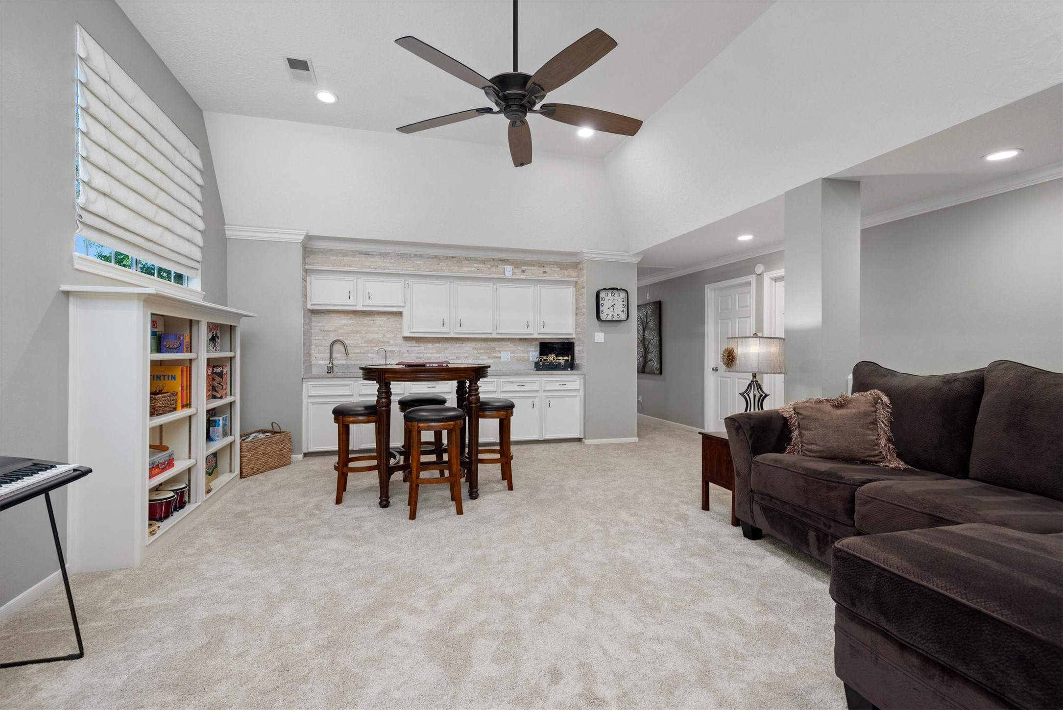 16022 Stewarts Grove Drive Spring, TX 77379 - Photo 27 of 45 GAME ROOM: 22’ X 15’ with 11’ ceiling height. This 2nd Floor living area boasts an angled tray ceiling, crown molding, granite countertops, and travertine accents. Custom wood cabinetry with a sink, under-cabinet LED lighting, neutral gray paint, beige roman shades, beige plush carpeting, and space for a game table or seating area make it a versatile space. It can be used as a game room, media room, or even a second family living area.