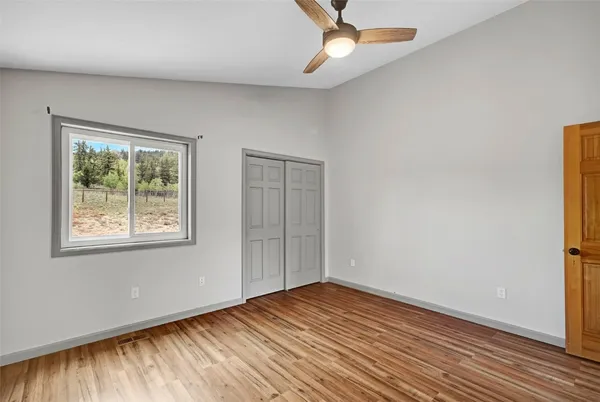 an empty room with wooden floor chandelier fan and windows