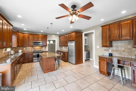 a kitchen with stainless steel appliances kitchen island granite countertop a refrigerator oven a sink a dining table and chairs with wooden floor
