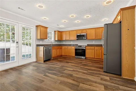 a kitchen with stainless steel appliances granite countertop a stove top oven a sink dishwasher a refrigerator and a dining table with wooden floor