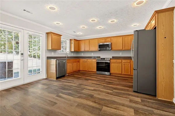 a kitchen with stainless steel appliances granite countertop a stove top oven a sink dishwasher a refrigerator and a dining table with wooden floor
