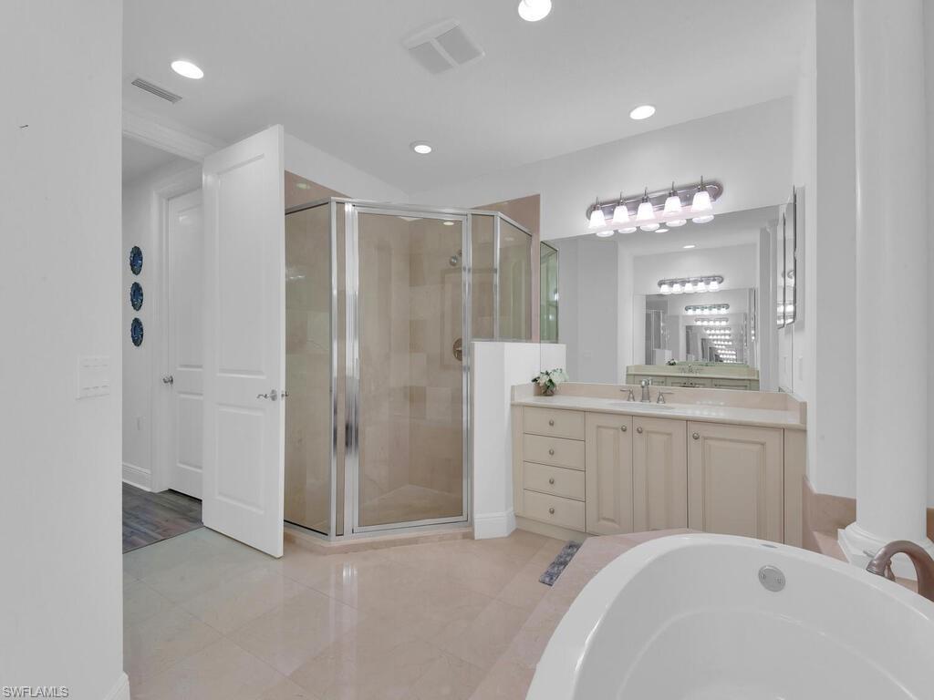 2710 Callista Court, Unit 104 Naples, FL 34114 - Photo 29 of 43 a spacious bathroom with a double vanity sink a mirror a bathtub and a shower