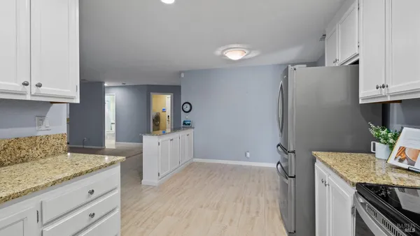 a kitchen with granite countertop a refrigerator a stove a sink and white cabinets with wooden floor