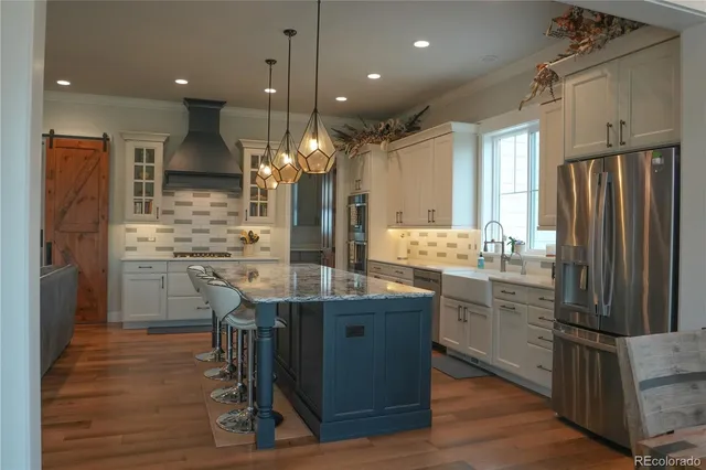 a kitchen with stainless steel appliances kitchen island granite countertop a refrigerator a stove and a wooden floors
