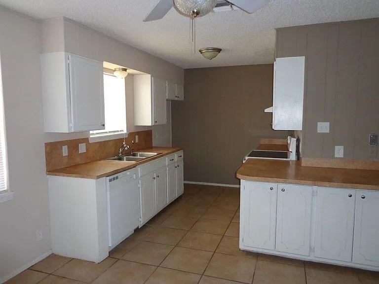 4004 Vicky Street Big Spring, TX 79720 - Photo 9 of 13 Kitchen featuring white cabinetry, light countertops, an undermount double-basin sink, and tile flooring