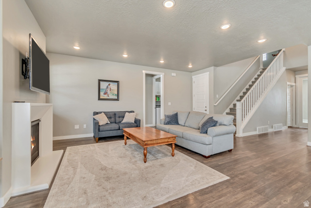 3232 West 1670th Street North Provo, UT 84601 - Photo 9 of 33 Living area with dark wood-style flooring, a lit fireplace, recessed lighting, and a textured ceiling