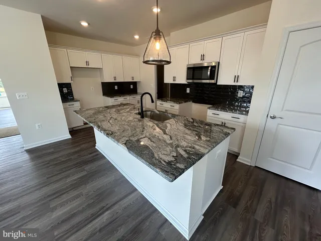 a kitchen with stainless steel appliances granite countertop a stove top oven a sink dishwasher and a microwave oven on the wooden floor