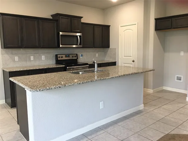 a kitchen with granite countertop a stove a microwave a sink and cabinets