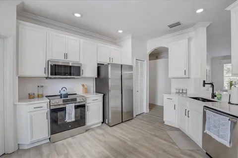 a kitchen with stainless steel appliances granite countertop a refrigerator stove a sink and white cabinets with wooden floor