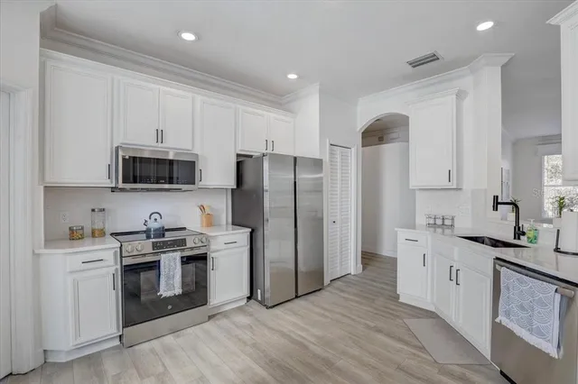 a kitchen with stainless steel appliances granite countertop a refrigerator stove a sink and white cabinets with wooden floor