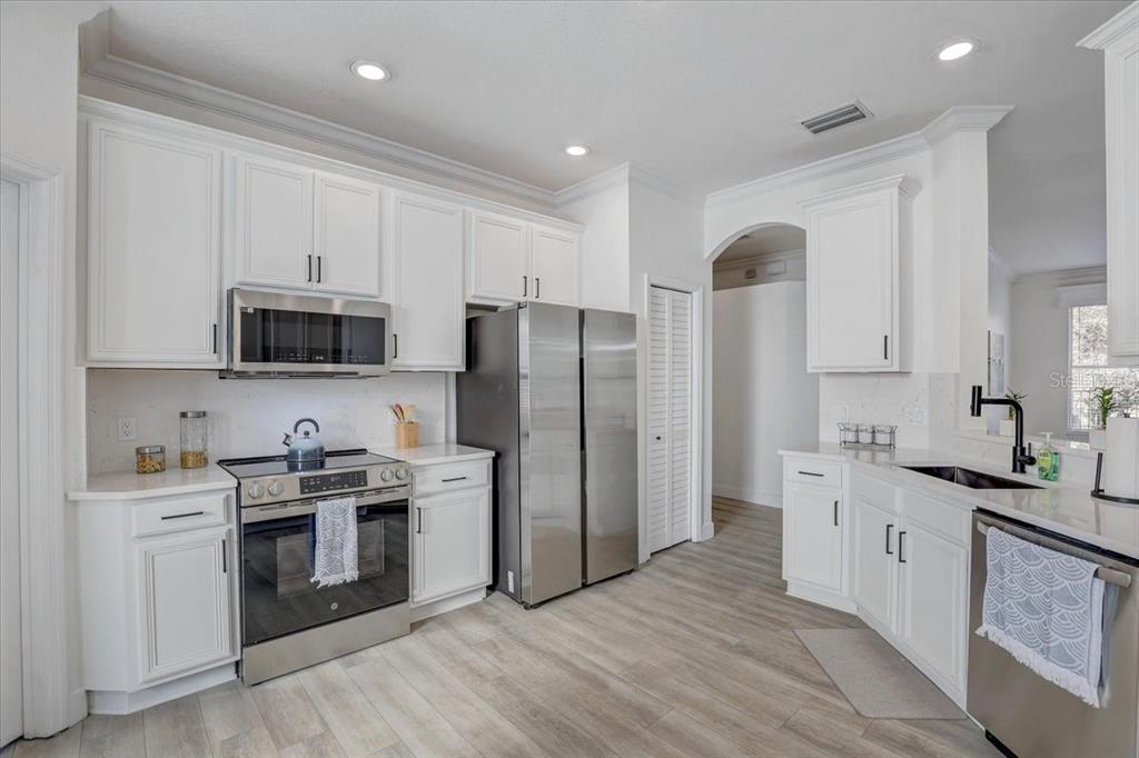 4006 91st Avenue East Parrish, FL 34219 - Photo 16 of 48 a kitchen with stainless steel appliances granite countertop a refrigerator stove a sink and white cabinets with wooden floor