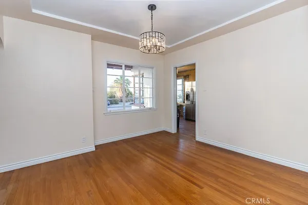 an empty room with wooden floor chandelier and windows