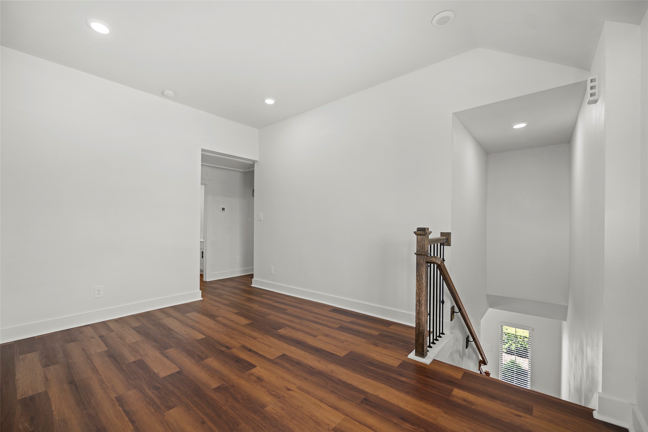10603 Whitejacket Conroe, TX 77385 - Photo 7 of 42 This photo showcases a bright, open upstairs area with modern laminate wood flooring, recessed lighting, and a staircase featuring a wooden handrail and metal balusters. The space is versatile, ideal for a game room or office