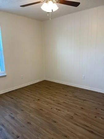 a view of an empty room with wooden floor and a chandelier fan