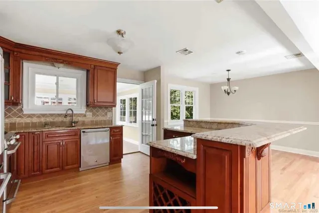 a kitchen with stainless steel appliances granite countertop wooden cabinets a sink a stove a dining table and chairs