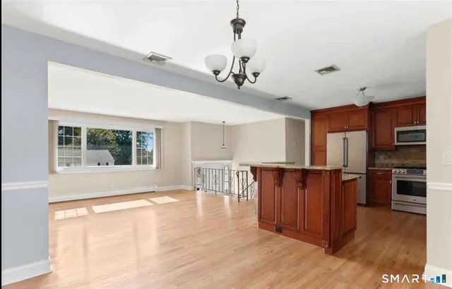 a open kitchen with stainless steel appliances granite countertop a stove top oven a refrigerator a dining table and chairs with wooden floor