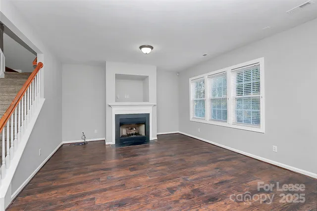 a view of an empty room with wooden floor fireplace and a window