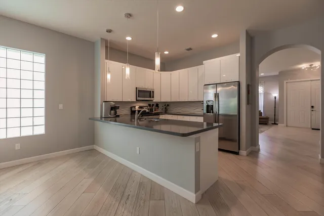 a kitchen with stainless steel appliances granite countertop a refrigerator a sink dishwasher a stove and white countertops with wooden floor