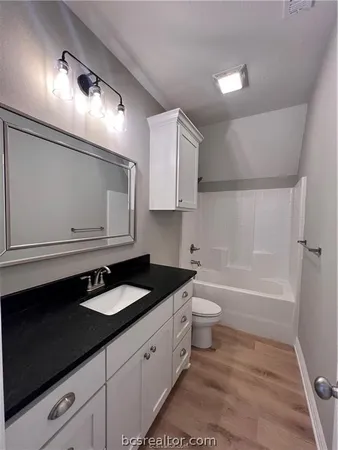 a bathroom with a granite countertop sink a toilet a mirror and bathtub
