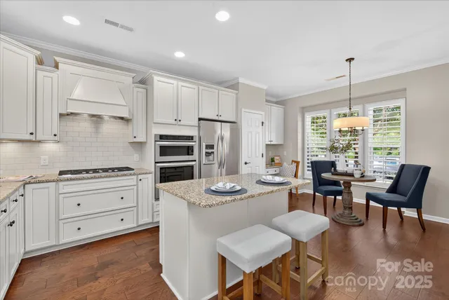 a kitchen with stainless steel appliances kitchen island granite countertop a stove a sink a dining table and chairs with wooden floor