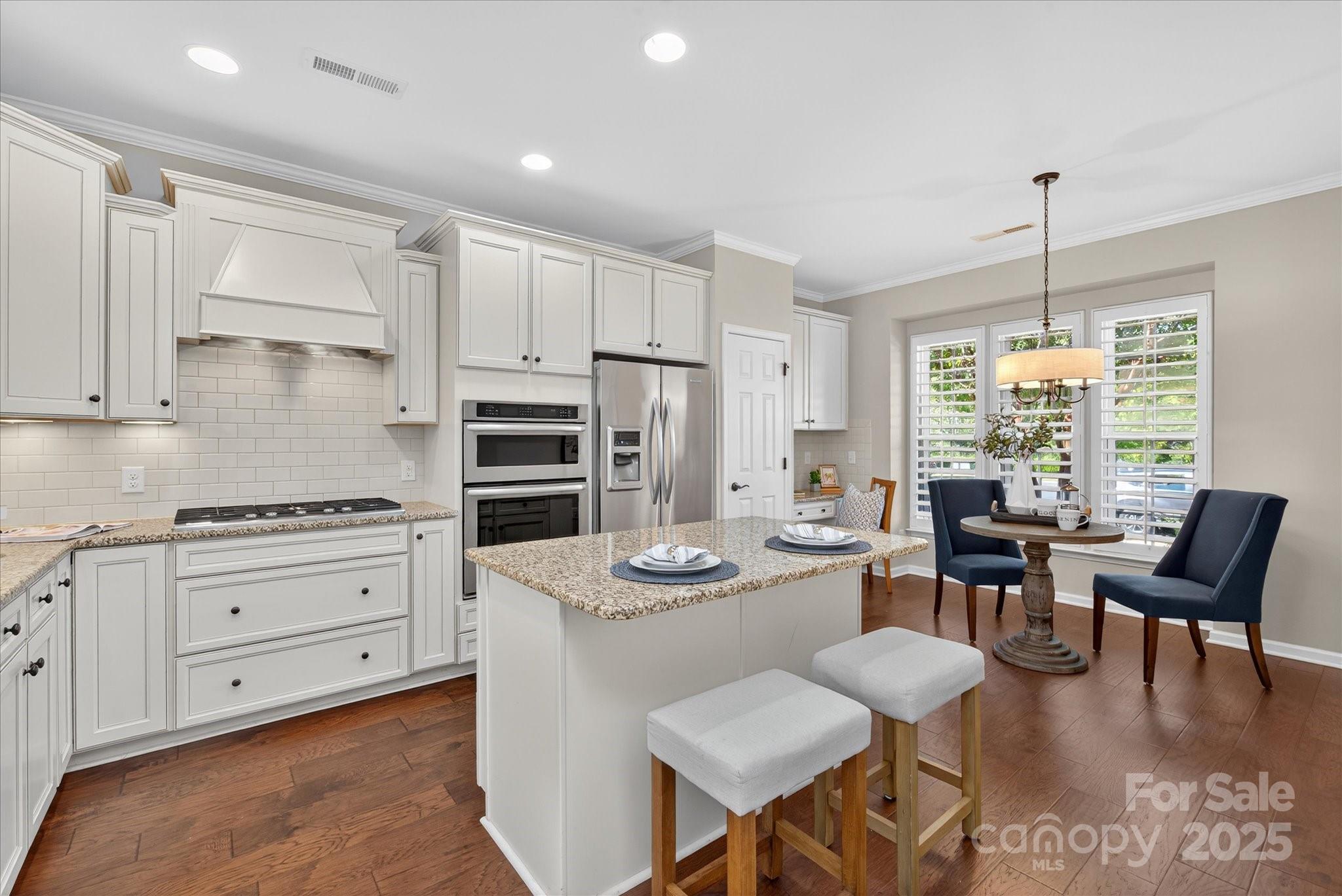 a kitchen with stainless steel appliances kitchen island granite countertop a stove a sink a dining table and chairs with wooden floor