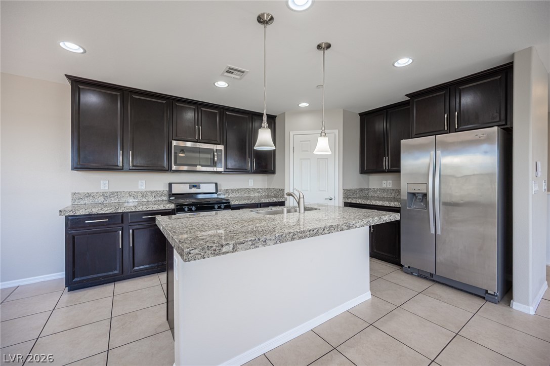 9916 Sable Point Street Las Vegas, NV 89178 - Photo 31 of 73 A contemporary kitchen features dark cabinetry, light granite countertops, and sleek stainless steel appliances.