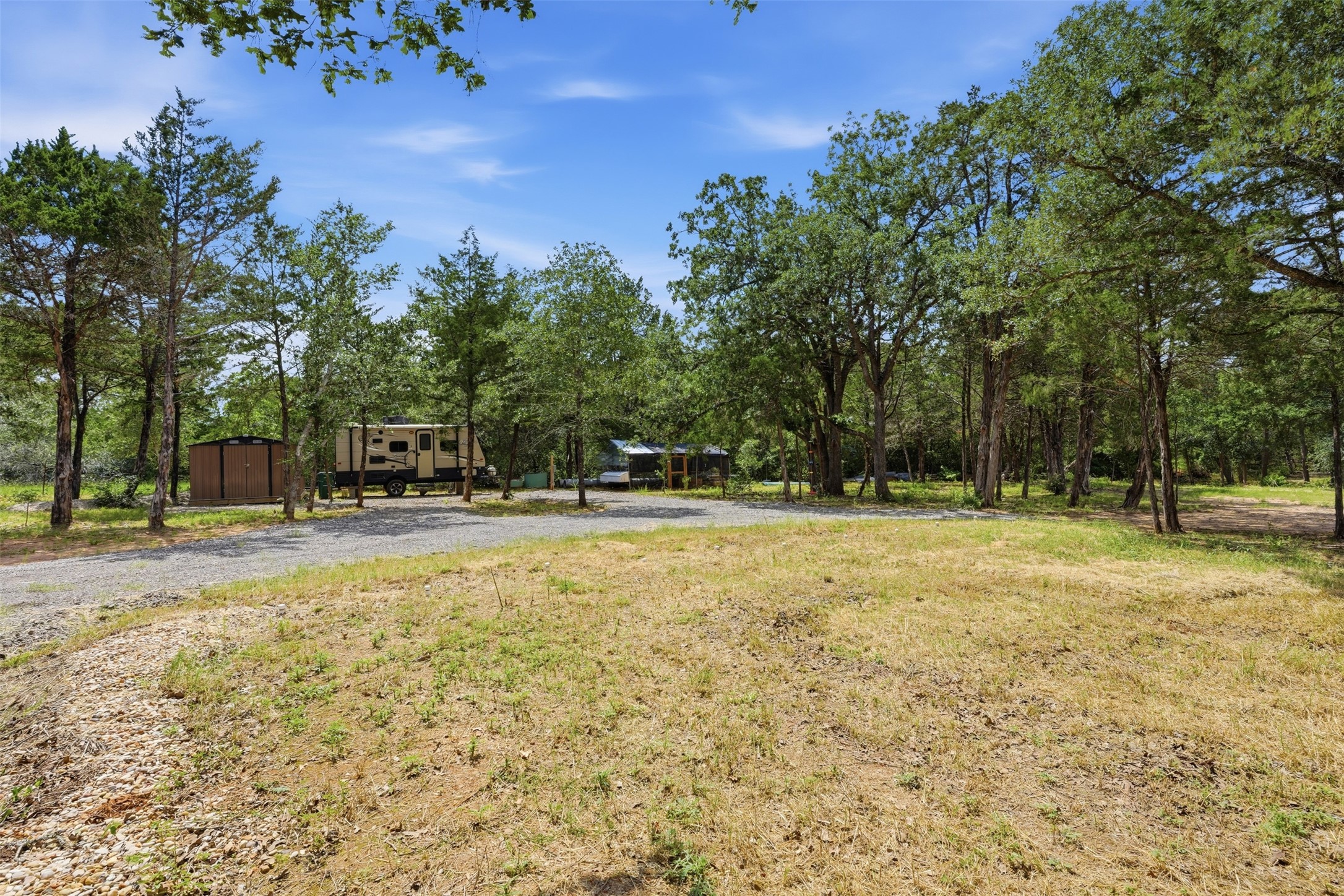 154 Antioch Road Smithville, TX 78957 - Photo 24 of 32 Mature trees frame a spacious lot with a gravel driveway, offering a serene, private setting.