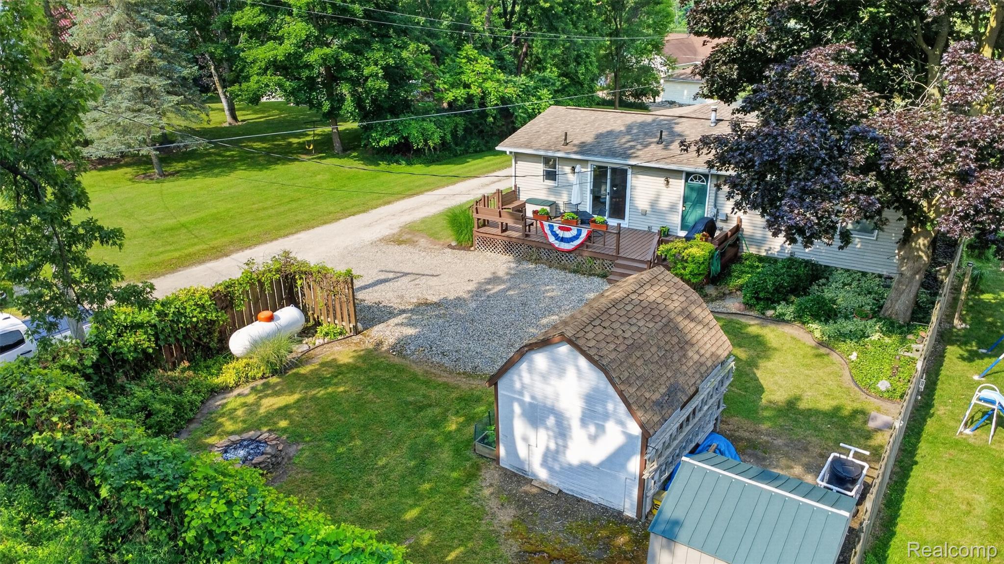 5977 Anglers Road Ortonville, MI 48462 - Photo 42 of 63 Rear exterior featuring a spacious wooden deck with direct access to the interior, a detached storage shed, and a stone fire pit area