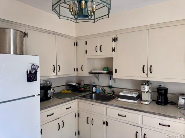Kitchen featuring white cabinetry with dark hardware, a stainless steel sink, and a stained glass-style ceiling light fixture