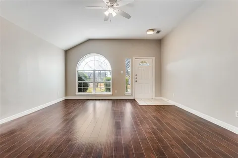 an empty room with wooden floor fan and windows