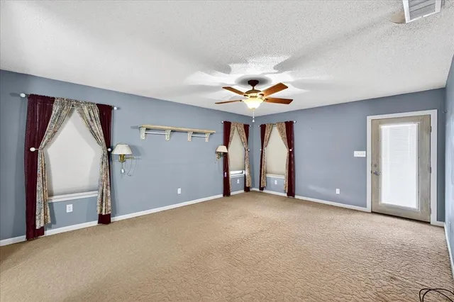 an empty room with chandelier fan and windows
