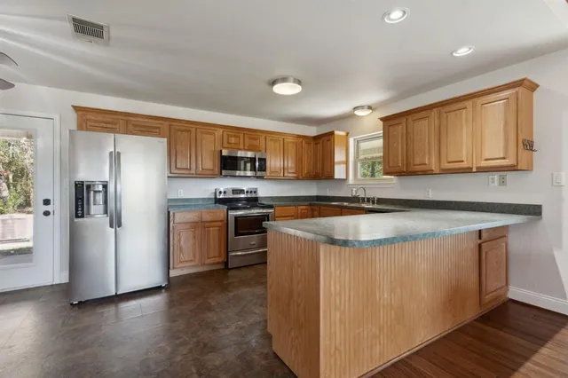 a kitchen with stainless steel appliances granite countertop a stove a sink dishwasher a refrigerator and a microwave oven with wooden floor