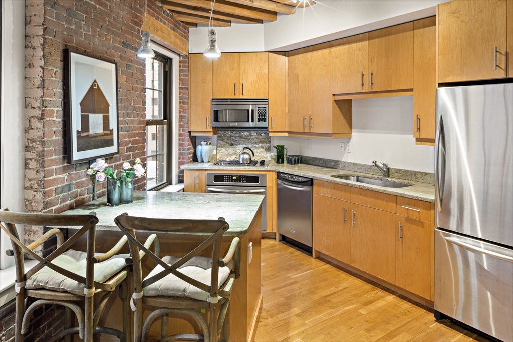 99-105 Broad Street, Unit 4F Boston, MA 02110 - Photo 7 of 16 a kitchen with stainless steel appliances a refrigerator a stove a sink dishwasher and white cabinets with wooden floor