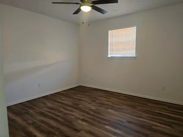 an empty room with wooden floor chandelier fan and windows