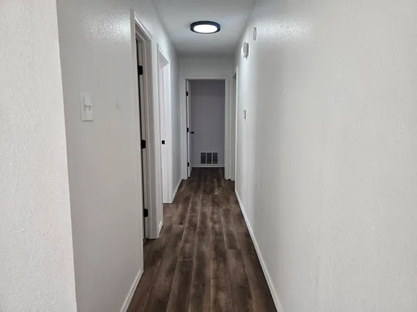 a view of a hallway with wooden floor and a bathroom