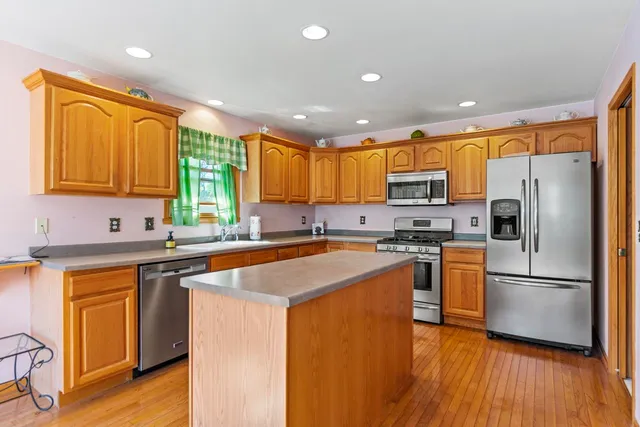 a kitchen with stainless steel appliances granite countertop a refrigerator a sink dishwasher a stove and white countertops with wooden floor