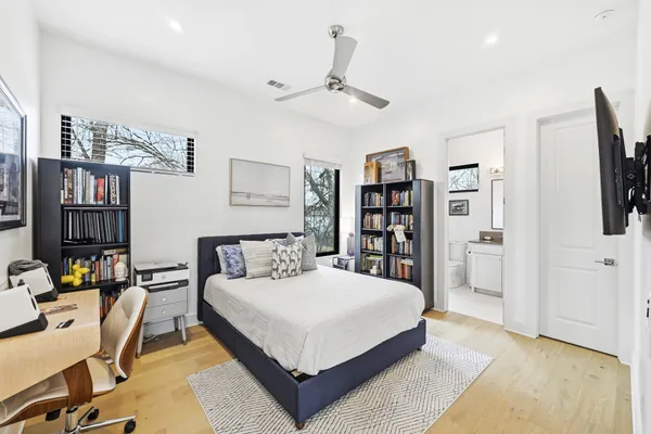 a bedroom with a bed a computer on the desk and a book shelf