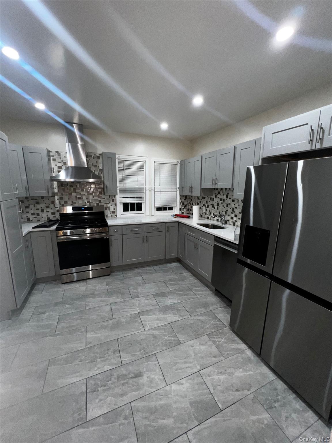 349 Warwick Avenue Mount Vernon, NY 10553 - Photo 4 of 15 Kitchen featuring stainless steel appliances, gray cabinets, wall chimney exhaust hood, backsplash, and recessed lighting