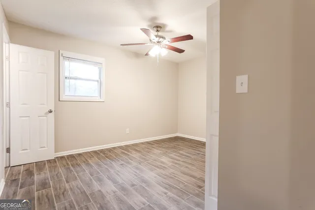 a view of an empty room with wooden floor and a ceiling fan