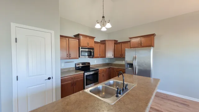 a kitchen with stainless steel appliances granite countertop a sink dishwasher a refrigerator and a stove with wooden floor