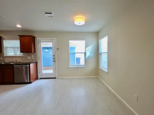 a view of an empty room with kitchen and window
