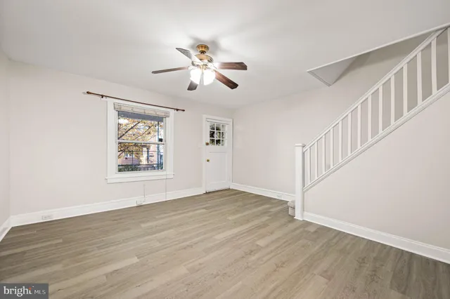 a view of an empty room with wooden floor and fan