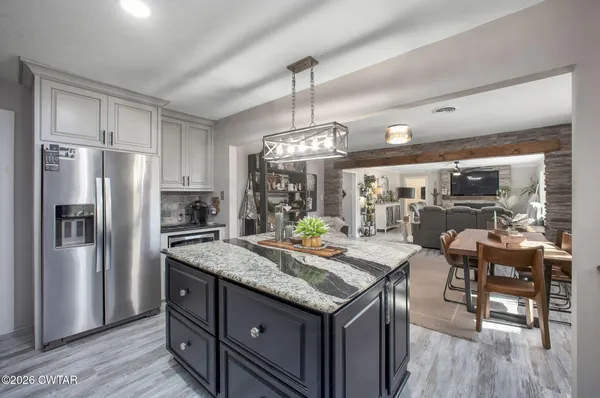 a kitchen with stainless steel appliances granite countertop a kitchen island a stove a refrigerator a oven a dining table and chairs with wooden floor