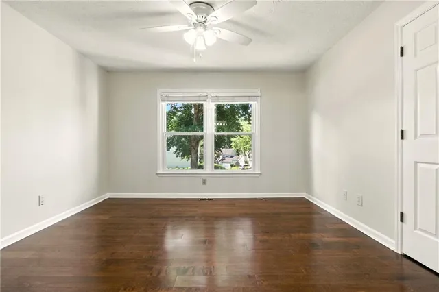 an empty room with wooden floor chandelier fan and windows